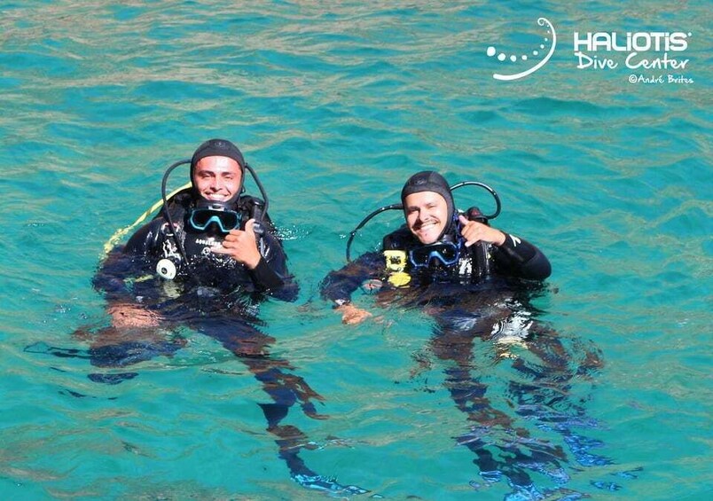 Two scuba divers in clear blue water, wearing black wetsuits and diving gear. 1