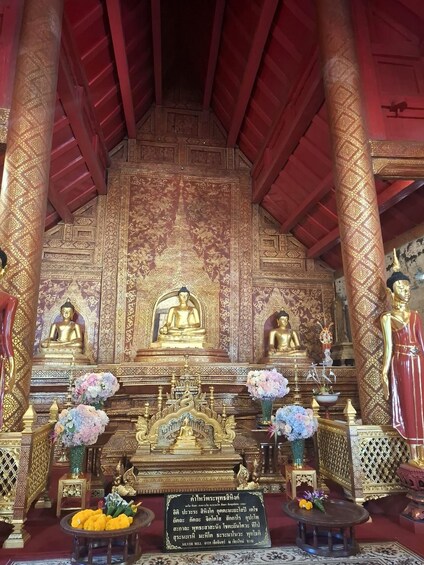 A temple interior with golden statues, intricate wall carvings, and floral arrangements. 5
