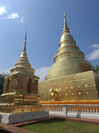 Two golden stupas with intricate designs, surrounded by a white fence and a well-maintained lawn. 3