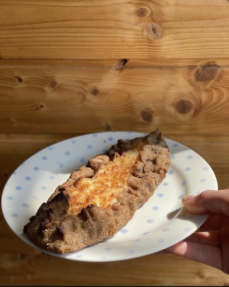 A hand holding a piece of fried food on a plate with a wooden background. 1