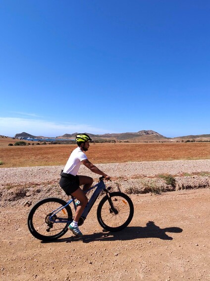 A person riding a bicycle on a gravel path with a clear blue sky and distant hills. 4