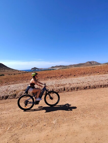 A person riding a bicycle on a dirt path with a clear blue sky and distant hills. 3