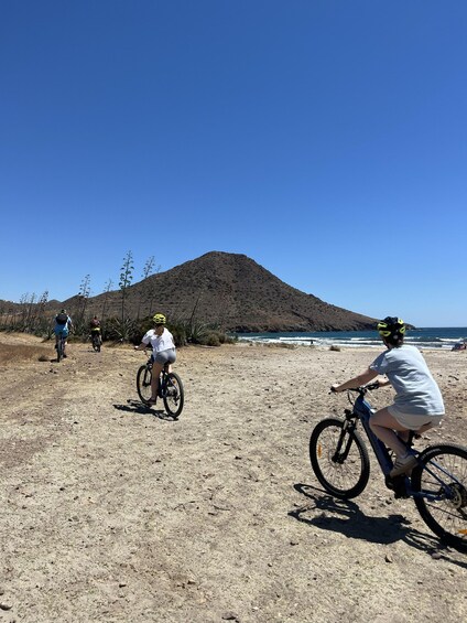 A group of cyclists on a dirt path with a mountain and ocean in the background. 2