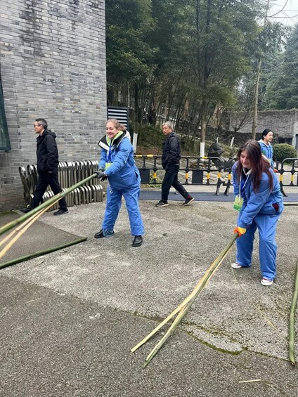 People in blue uniforms cleaning a paved area with brooms and a hose. 5