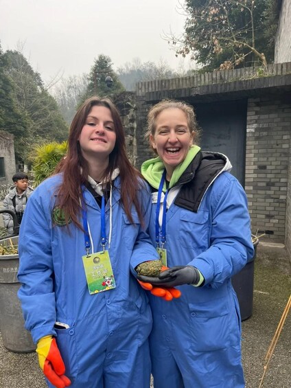 Two individuals in blue work uniforms holding tools and materials, standing in an outdoor setting with a brick wall and trees in the background. 3