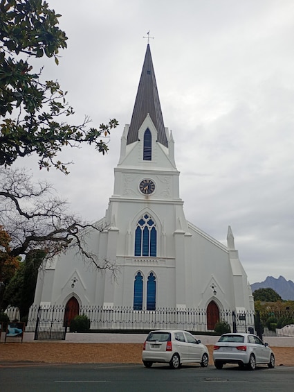 A white church with a pointed steeple, a clock, and two blue windows. 5