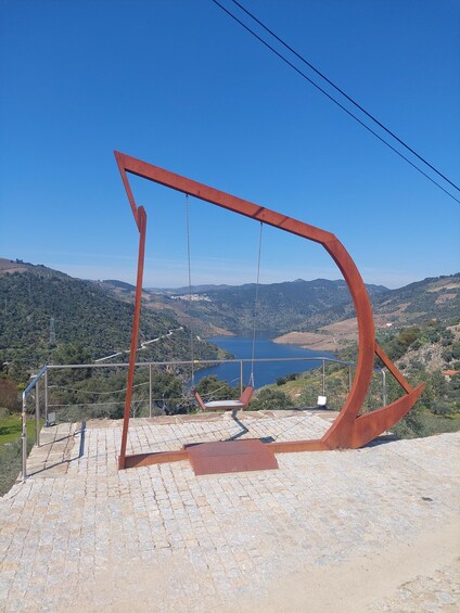A metal sculpture with a swing, overlooking a valley with a lake and hills. 4