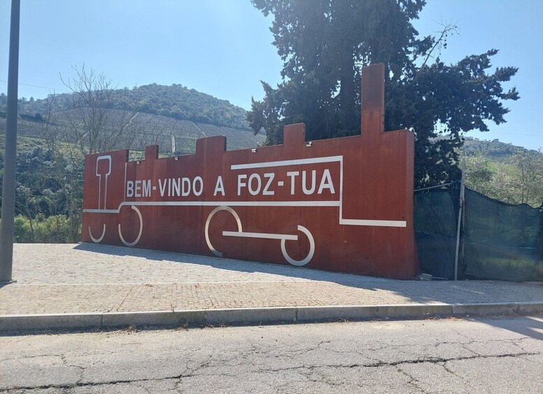 A red sign with white text reading 'Bem-Vindo A Foz-Tua' and a train silhouette. 5