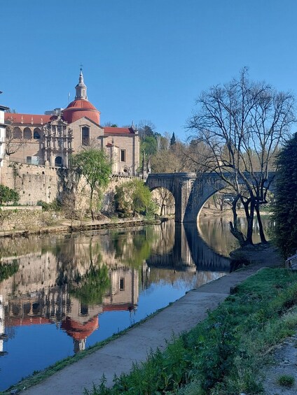 A historic building with a red dome, a stone bridge, and a calm river reflecting the structure. 1