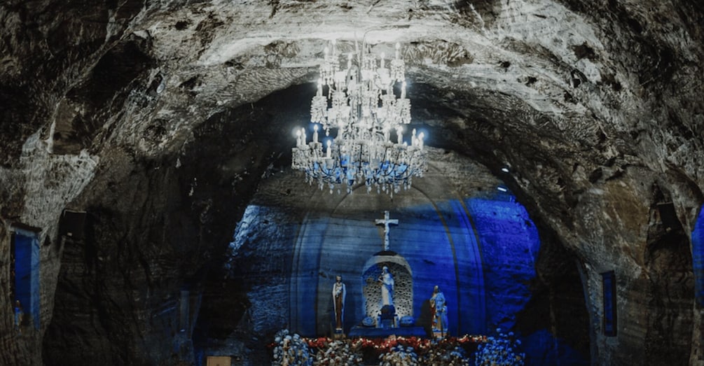An interior of a cave church with a chandelier, altar, and religious statues. 2