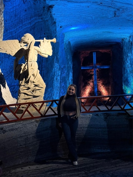 A person standing in front of a cave with a blue-lit interior and a large statue. 1