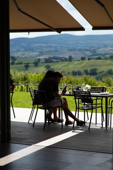 A couple seated at an outdoor table with a view of rolling hills and vineyards. 2