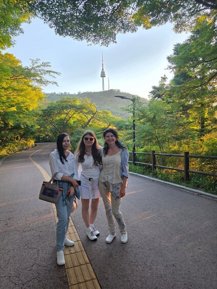 Tres personas de pie sobre un sendero empedrado, con árboles y una torre al fondo. 1
