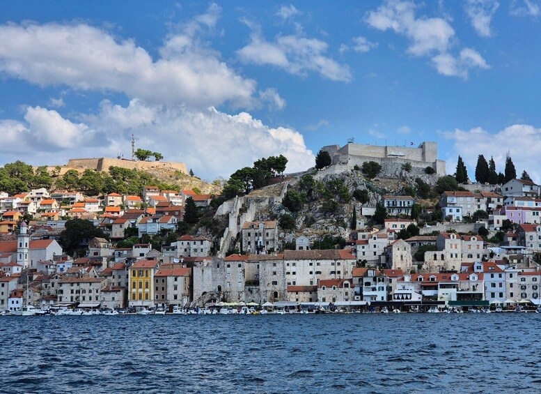 A coastal town with historic stone buildings, a prominent castle on a hill, and a marina with boats. 4