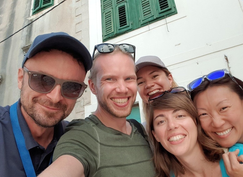A group of people taking a selfie in front of a building with green shutters. 1