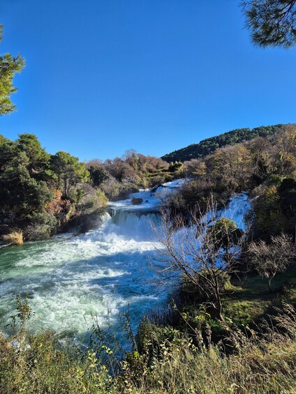 A river with a waterfall surrounded by trees and hills. 3