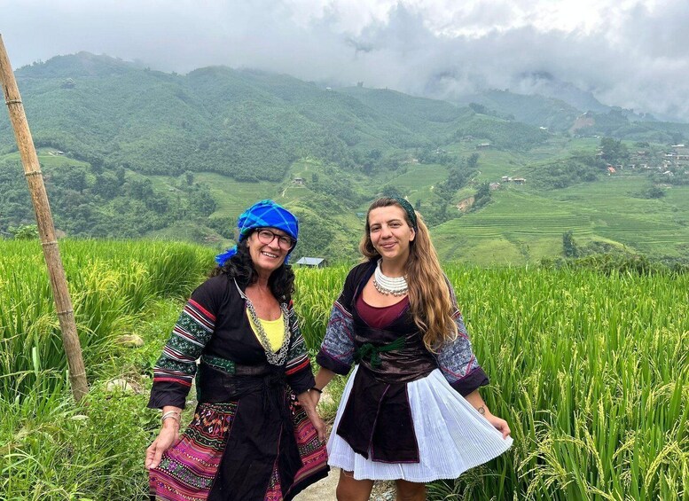 Two people in traditional attire standing in a rice field with a mountainous landscape in the background. 4