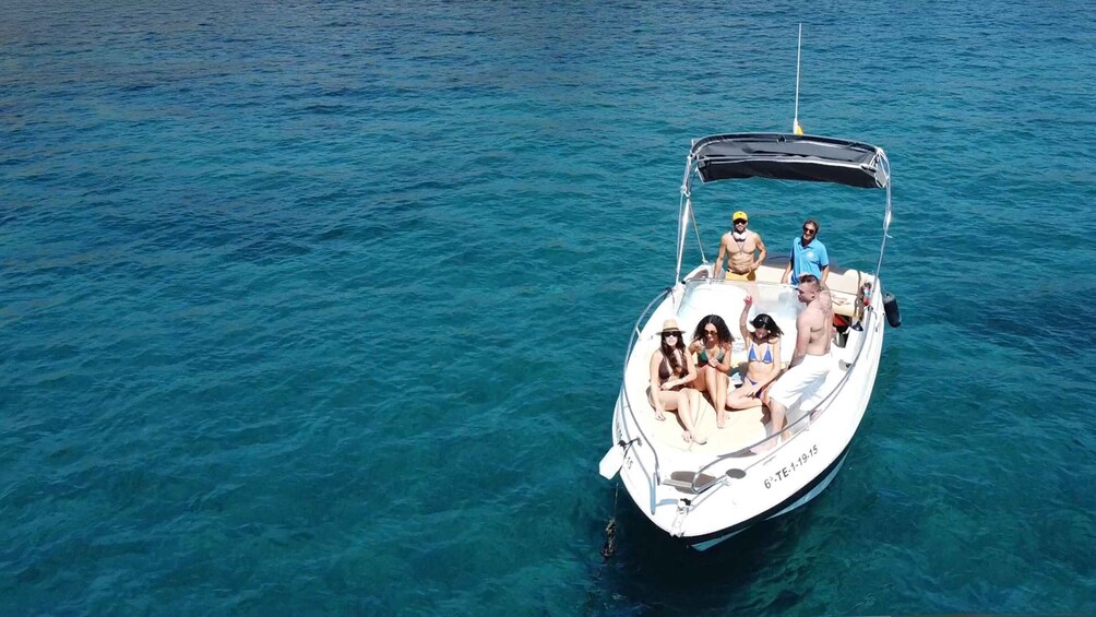 A small white boat with people on board, floating on clear blue water. 5