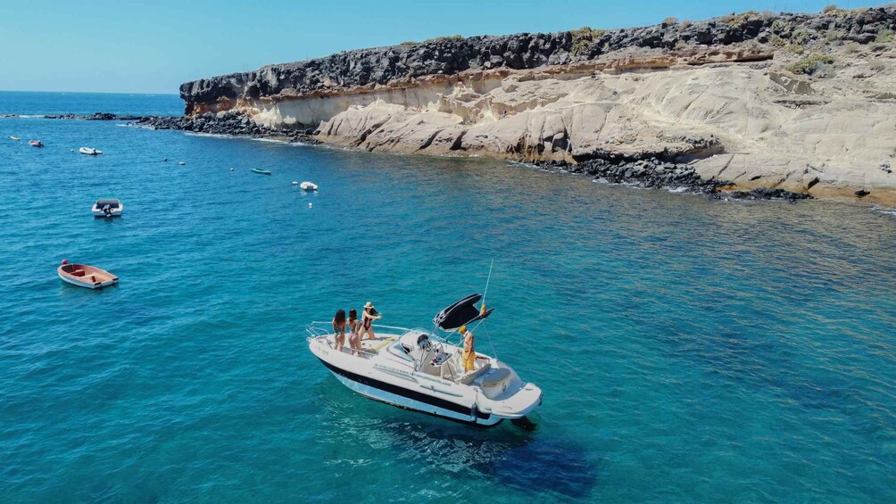 A clear blue sea with boats, rocky cliffs, and a calm shoreline. 1