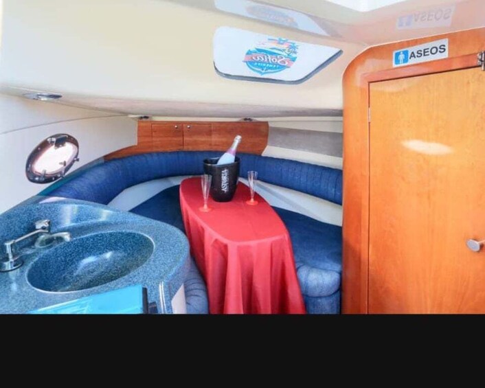 A compact boat interior with a blue cushioned seating area, a small table with a red cloth, a sink, and a wooden cabinet. 5