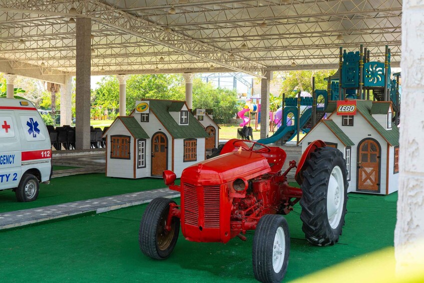 Un tractor rojo, una ambulancia blanca y una estructura de juegos verde en un espacio cubierto con piso verde. 4