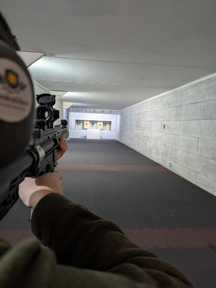 A person aiming a rifle at a shooting range with targets in the distance. 1