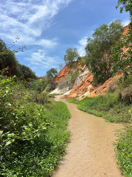 A dirt path winding through a lush green landscape with red rock formations. 1