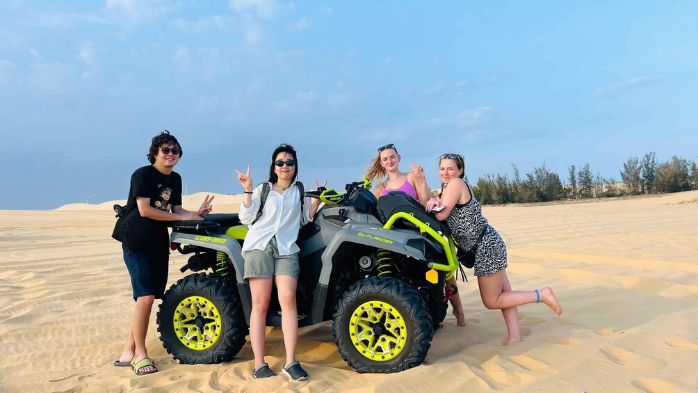 Four people posing with a quad bike in a desert. 3