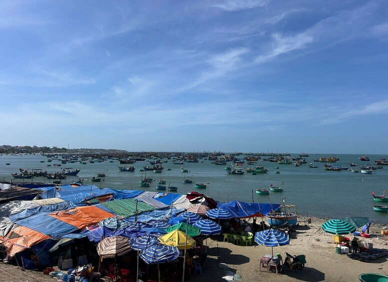 A coastal area with numerous boats on the water and a beach with colorful umbrellas and makeshift stalls. 5