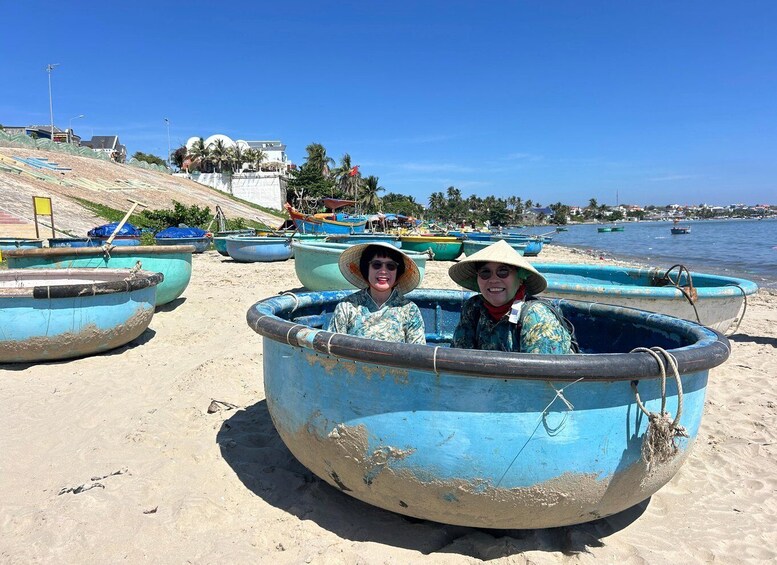 Two people in a blue boat on a sandy beach with other boats and a clear blue sky in the background. 2
