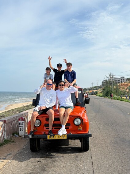 A group of people on a red vehicle parked on a road by the beach. 4