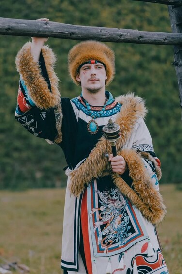 A person in traditional attire holding a staff, standing in a natural outdoor setting. 2