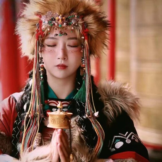 A person in traditional attire with a fur-lined hat, colorful beaded jewelry, and a prayer-like gesture. 4