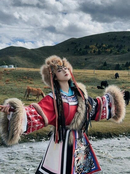 A person in traditional attire with fur details, standing in a rural landscape with hills and grazing animals. 3