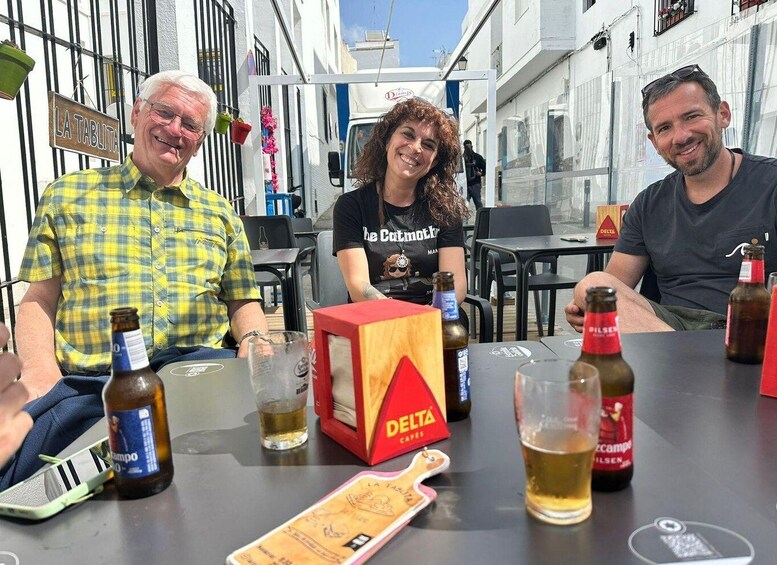 Three people seated at an outdoor table with drinks and a Delta Capes box. 1