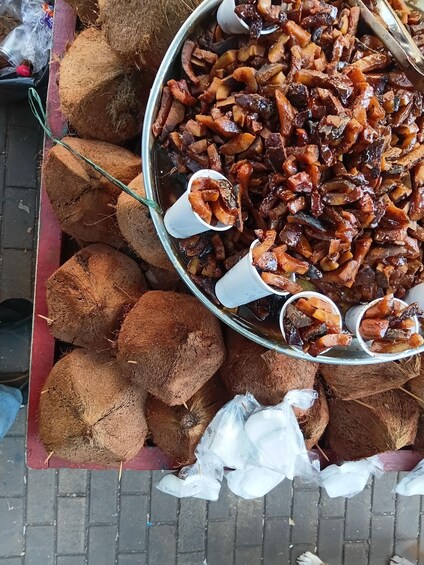A metal tray filled with cooked meat and coconut shavings, with small white cups on top. 4