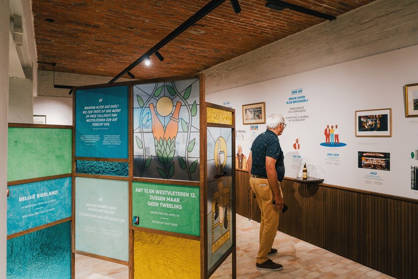 A man standing in a room with a wall displaying various framed pictures and text panels. 5