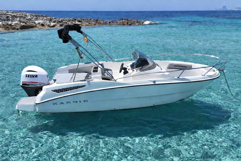 A white motorboat named 'KARNIC' anchored near rocky shores in clear turquoise waters. 2