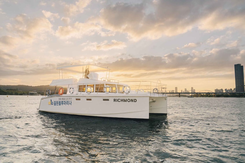 A white boat named 'RICHMOND' on water with a city skyline and a bridge in the background. 1