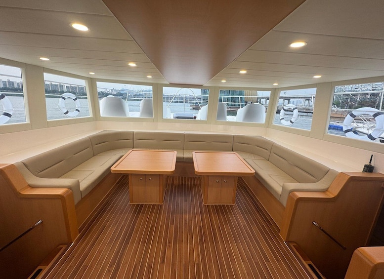 A boat interior with a wooden deck, cushioned seating, and large windows overlooking a marina. 4