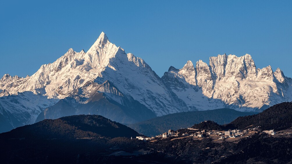 A snow-covered mountain range with a small settlement at its base. 2