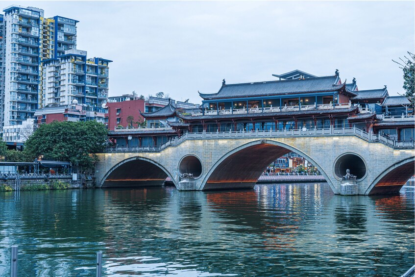 A traditional bridge with multiple arches over a river, with modern buildings in the background. 3