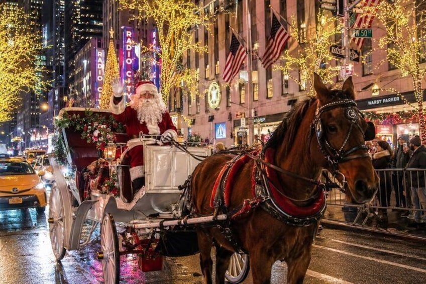 A horse-drawn carriage with a person in a Santa costume, decorated with lights and flowers, on a city street at night. 3