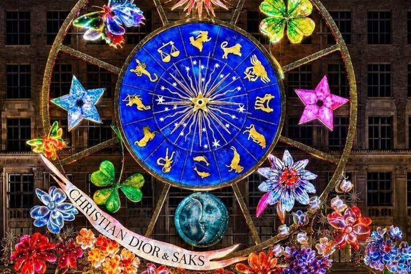 A large, ornate wheel with zodiac symbols and floral decorations, set against a building facade. 1