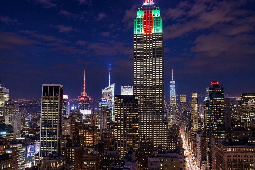 A nighttime cityscape with illuminated skyscrapers, including a prominent building with red, green, and white lights at the top. 5