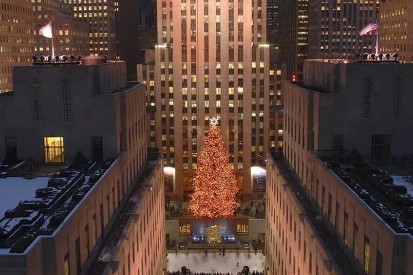 A large illuminated Christmas tree in a city plaza surrounded by tall buildings. 4
