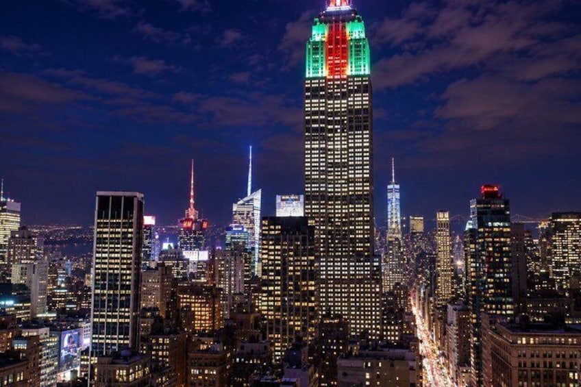 A city skyline at night with illuminated buildings, including a prominent skyscraper with red, green, and white lights at the top. 5