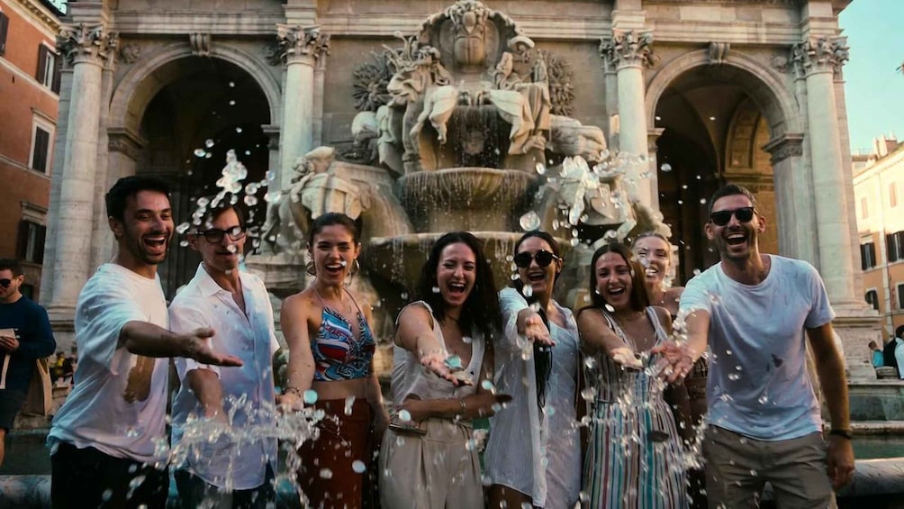 A group of people throwing water at a fountain in front of a historic building. 3