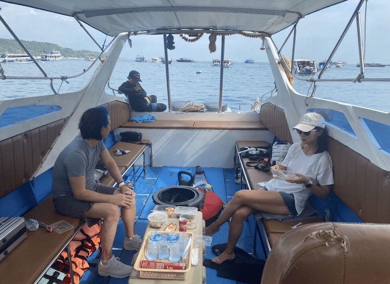 A boat with two people seated at the stern, a table with food and drinks, and a view of the sea with other boats in the distance. 3