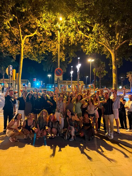 A group of people posing for a photo in an outdoor setting at night with street lamps and trees. 4